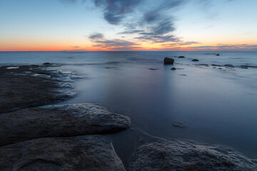 Fototapeta na wymiar Twilight sunset over rocky shore of Baltic sea. Almost clear sky and orange strap along the horison. Estonia.