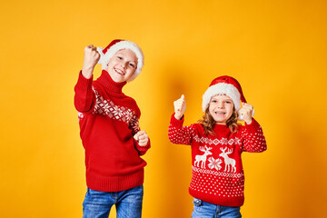 Happy children in red sweaters with deer having fun and showing thumbs up on Christmas day against yellow background
