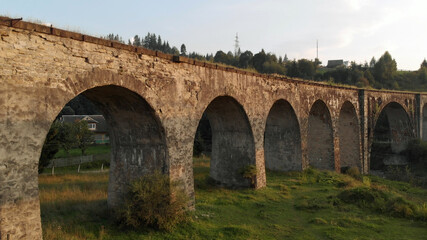 Fototapeta na wymiar Ancient bridge in mountain village. Summer landscape of abandoned railway bridge.