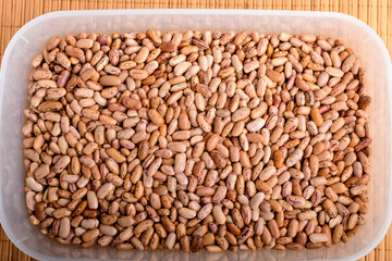 Natural background of many fresh organic red beans in a plastic box in warm light, top view or flat lay of organic vegan food photographed with soft focus