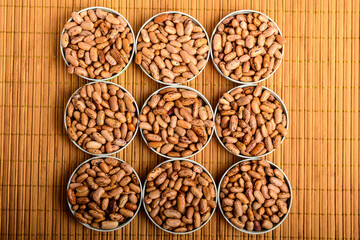 Top view of nine round bowls with many fresh organic red beans on a wooden table in warm light,...