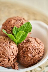 Chocolate ice cream with mint leafe. three balls in a white bowl on a vintage table.