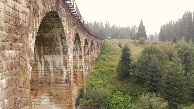 Close view of viaduct arches. Railroad on the bridge. Green hills with spruces on the background. © DenisProduction.com