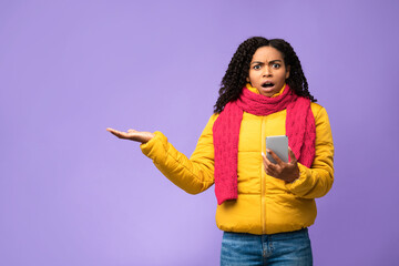 Shocked African Woman With Smartphone Gesturing At Copyspace, Purple Background