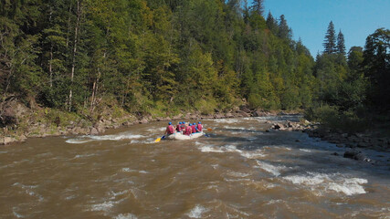 A white boat on the river. A dense green forest around. People are rafting on the cold mountain water.