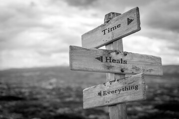 time heals everything text quote on wooden signpost outdoors in black and white.