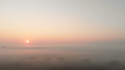 Beautiful sunrise landscape. The sun shining through the white thick fog. Purple dull sunshine in the morning sky.