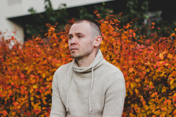 a man looks thoughtfully into the distance against a background of autumn leaves