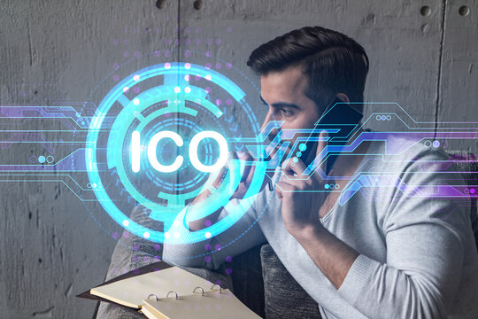 Handsome analyst in casual long sleeve talking phone, taking notes at office workplace try to analyze ICO project. Double exposure. Initial coin offering hologram. - Powered by Adobe