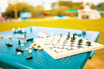 Chess and checkers are scattered on the table in the park. An intellectual game for developing strategy and tactics. Useful pastime on street. Resort entertainment. Chessboard and pieces on table.