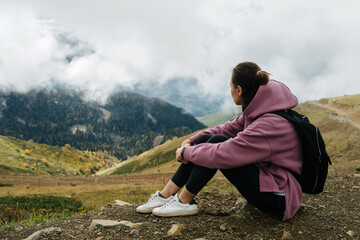 Immersed woman sitting on the ground high up in cloudy mountains.