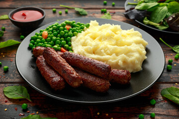 Vegetarian vegan sausages with mashed potato and green peas in black plate