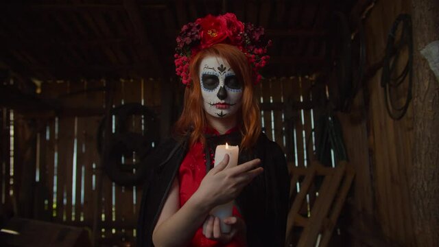 Creepy mysterious our lady of holy death, santa muerte with sugar skull and wreath, gesturing and putting out burning candle as symbol of human soul and safe departure of deceased to afterlife.