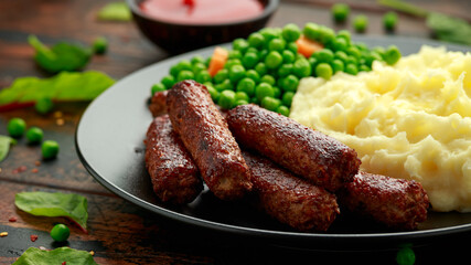 Vegetarian vegan sausages with mashed potato and green peas in black plate