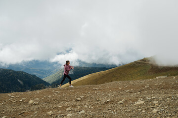 Far away shot of young woman running high up in cloudy mountains. Side view.