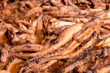 Octopus cooked with tomato sauce in a large traditional black fry pan at a street food festival, ready to eat seafood, side view.