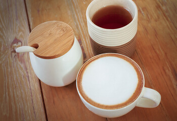 Cappuccino coffee cup, tea cup and sugar jars on wooden table.