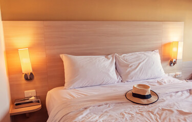 The white bed in the hotel has a tourist hat on it.