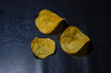 Three potato chips on a black background.