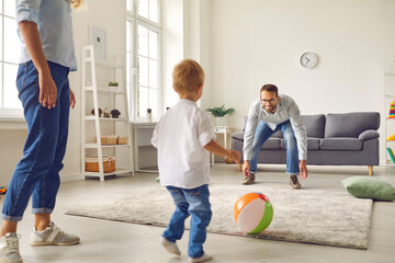Happy young dad, mum and little son playing football with inflatable ball in living-room