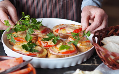 Elderly woman prepares to meet friends and made hot sandwiches with cheese, tomatoes, sausage on toast.Healthy natural food.