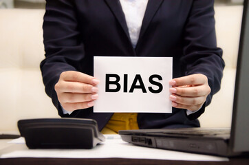 Obraz premium the word bias is written on a white piece of paper held by a business woman. personal opinions prejudice bias concept,