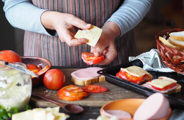 Home cooking. Elderly woman prepares to meet friends and prepares hot sandwiches with cheese, tomatoes, sausage on toast. Healthy natural food.