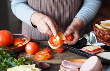 Home cooking. Elderly woman preparing hot sandwiches with cheese, tomato, sausage on toast for breakfast.Healthy natural food.