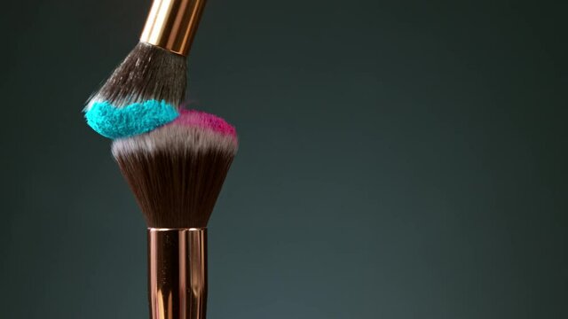 Makeup brushes touch each other on dark background and small particles of cosmetics, super slow motion, 1000 fps.