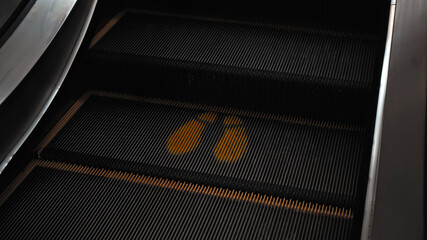 staircase escolator in a shopping center with a footprint sign for keeping a social distance