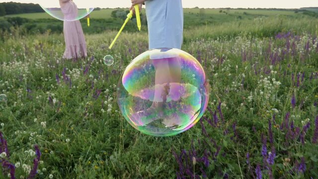 Close-up large soap bubbles burst hitting the grass, mom and children play with soap bubbles in the meadow in nature, slow motion
