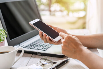 Young woman using smart phone and laptop with cup of coffee at home with copy space