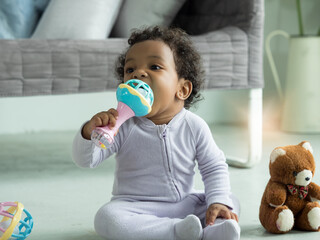 Cute little Black baby boy putting rattle toy into mouth.