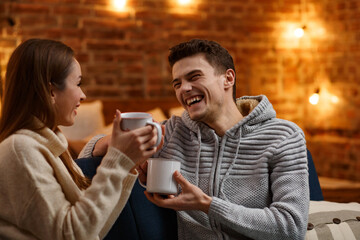 Beautiful young couple at home drinking coffee at Christmas morning. Spending time together, relationships and people concept. Winter holidays, Christmas celebrations, New Year concept.