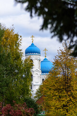 Christian Cathedral with blue domes among autumn trees against a blue sky with clouds