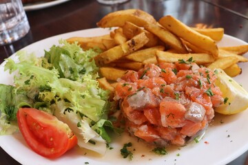 Tartare de saumon accompagné de frites et de salade dans une assiette blanche, saumon cru assaisonné, ville de Lyon, département du Rhône, France