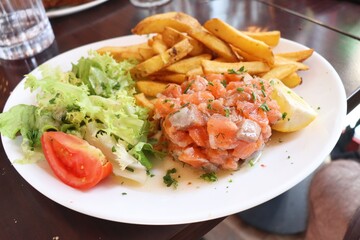 Tartare de saumon accompagné de frites et de salade dans une assiette blanche, saumon cru assaisonné, ville de Lyon, département du Rhône, France