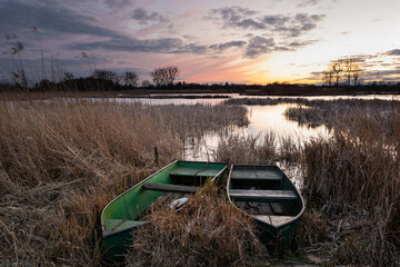 Anglers boats in reeds on the lake shore and the evening sky after sunset