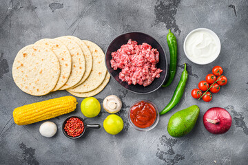 Raw organic mexican tacos ingredients with tortilla chips, avocado, salsa, chilli and meat. On grey concrete background, top view.