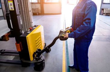 A worker in a warehouse uses a hand pallet stacker to transport pallets.