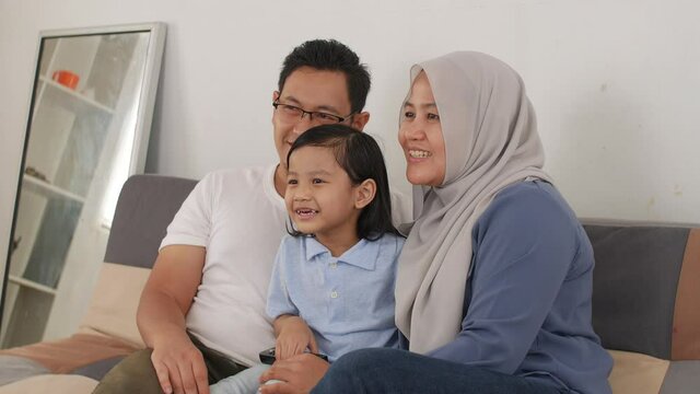 Happy muslim family watching tv. Asian father and mother spending quality time with their baby girl daughter watching movie at home 