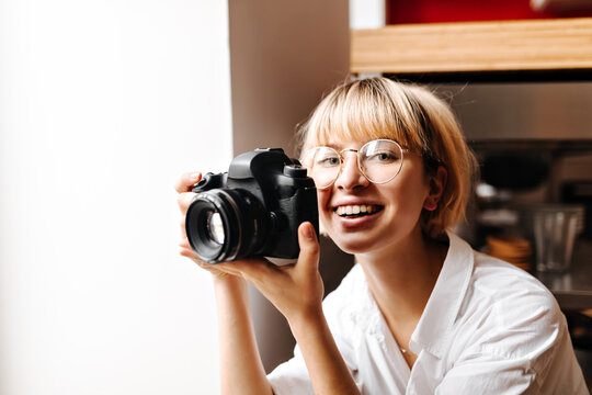Excited blonde girl taking photos. Laughing photographer in glasses holding camera.