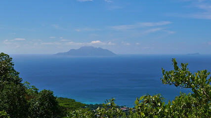 Fototapeta na wymiar Panoramic view from Dans Gallas hiking trail in the north of Mahe, Seychelles over the northern coastline with the silhouettes of Silhouette Island and Ile du Nord on the horizon.