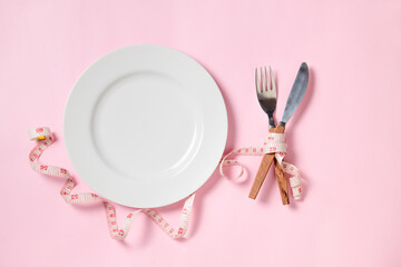 Empty white plate with a knife and fork wrapped in measuring tape on pink background.