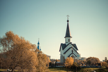 Obraz premium Two beautiful and different churches among autumn trees on a warm Sunny autumn day.