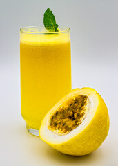 Passion fruit juice. Glass of passion fruit juice with mint leaf on the edge of the glass and half a passion fruit cut next to the glass, isolated on white background.