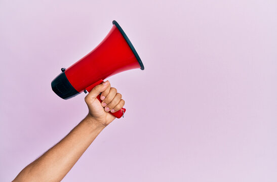 Hand of hispanic man holding megaphone over isolated pink background.