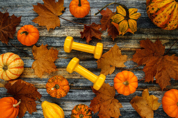 Two yellow dumbbells with various pumpkins, squashes and autumn leaves. Healthy fitness lifestyle...