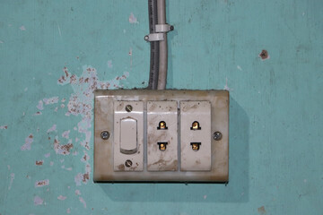 An old electrical switchboard with sockets attached to the painted wall. Aged power switch and output sockets