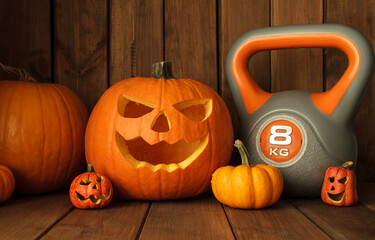 Heavy kettlebell with Halloween pumpkins on wooden background. Healthy fitness lifestyle autumn...